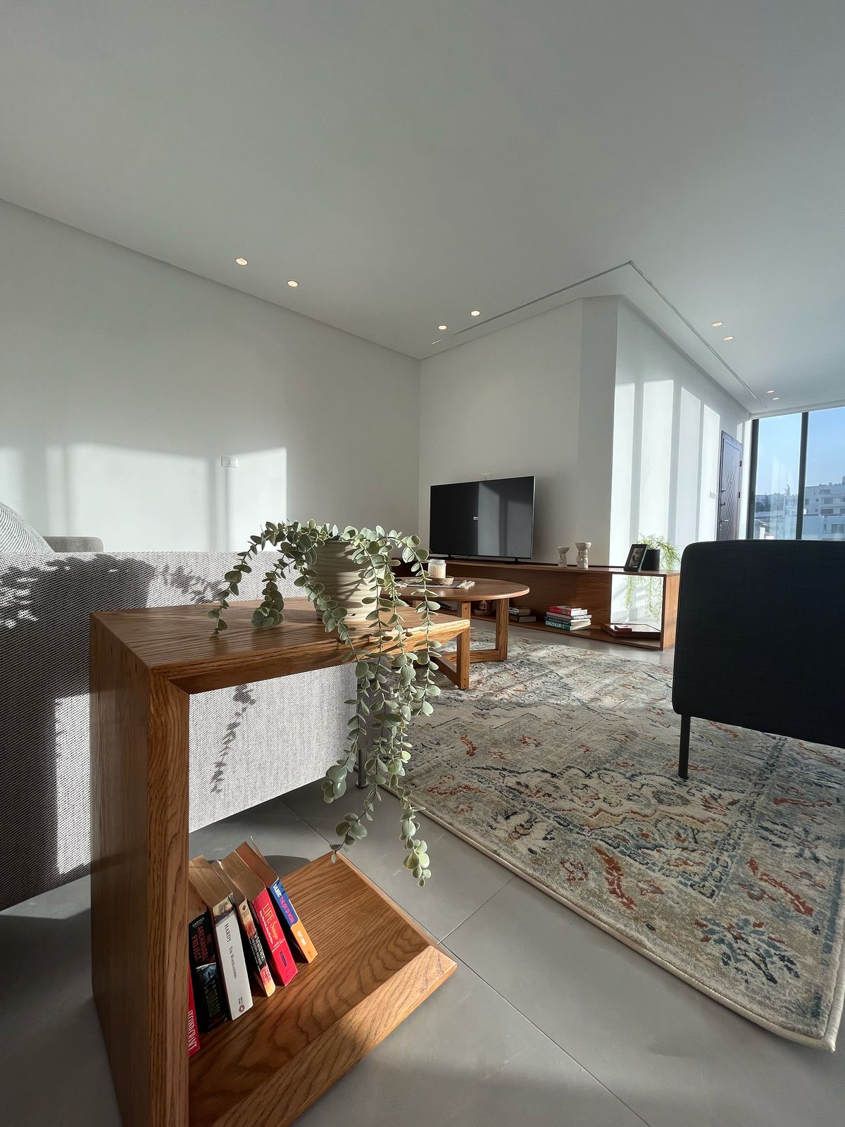 b00fdb75-be96-4951-a542-de85d460aade Modern living room with a wooden console table, trailing plant, and a rug beneath a sofa and TV stand.