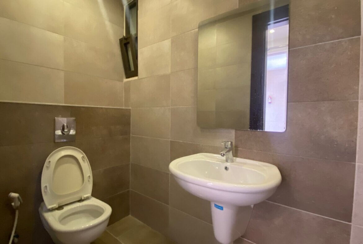 b2ff3316-fb81-46ee-9ab5-f9c51297df57 Bathroom with wall-mounted toilet and pedestal sink, rectangular mirror, and a spray bottle on a shelf nearby.