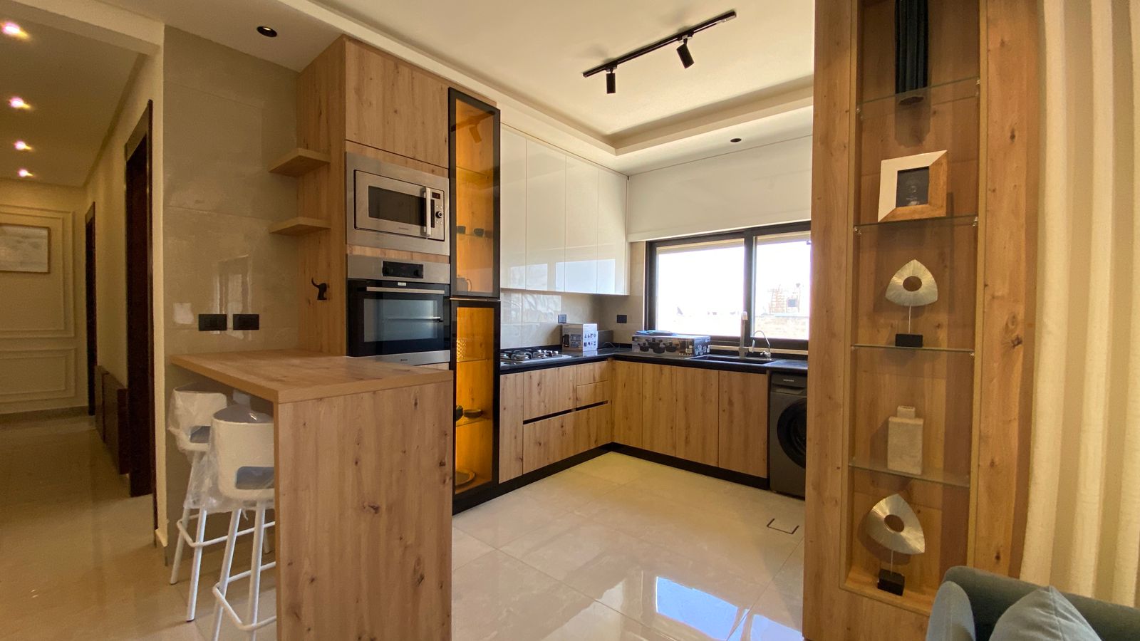 b41c1299-73c0-484f-afa3-9b79a2b30878 Modern L-shaped kitchen with warm wood cabinets, built-in ovens, and a breakfast bar with stools.