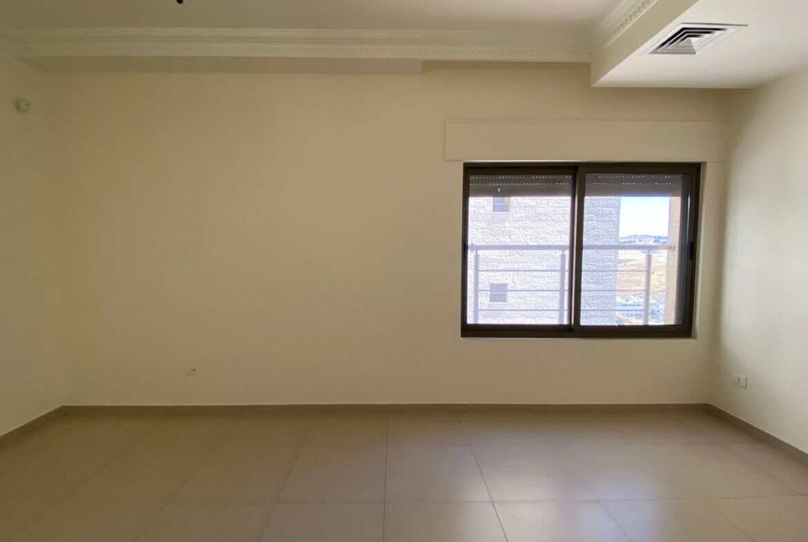b57fb540-128c-48c3-b8d4-d6dbd4410c2f Empty room with beige walls, tiled floor, decorative crown molding, and a large window letting in light.