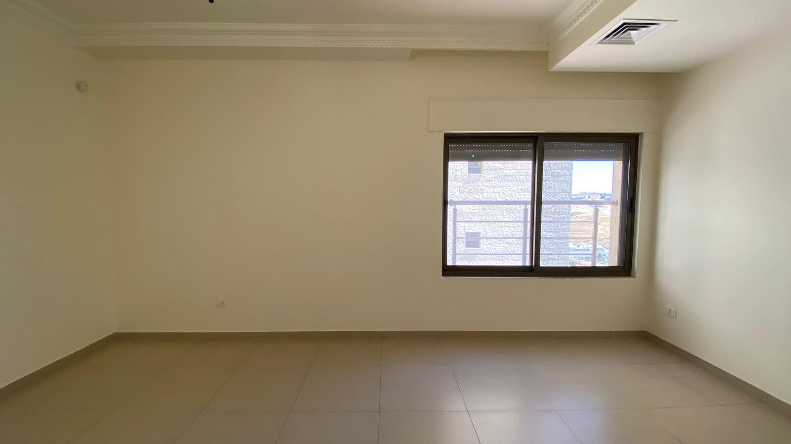 b57fb540-128c-48c3-b8d4-d6dbd4410c2f Empty room with beige walls, tiled floor, decorative crown molding, and a large window letting in light.