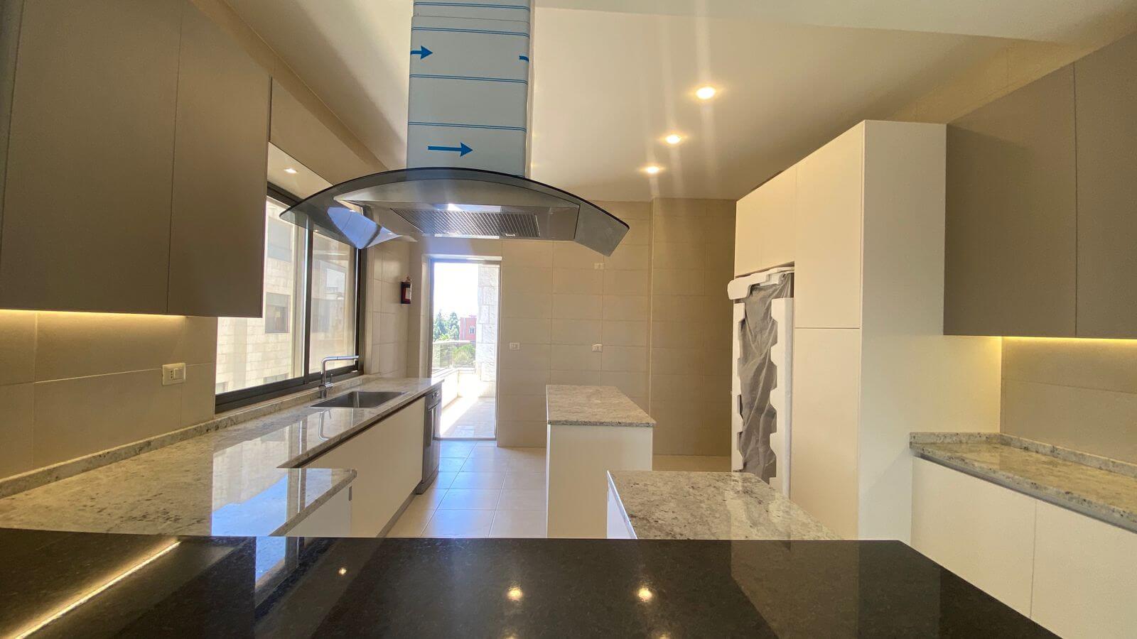 b6c53377-5545-46cb-924c-a0503a698f52 Bright modern kitchen with white cabinets, granite countertops, an island, and a curved glass range hood under a tall vent duct marked with blue arrows.