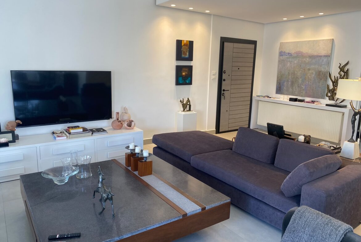 Living room with a wall-mounted flat-screen TV on white cabinets, decorative vases, and a dark blue sectional sofa facing the TV.