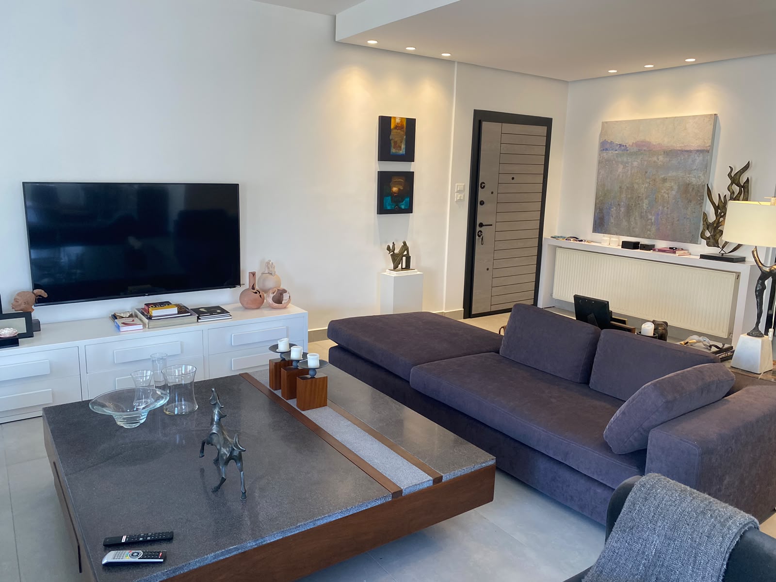 ba7d16e9-884a-4b2b-89c3-5132e8ade5ac Living room with a wall-mounted flat-screen TV on white cabinets, decorative vases, and a dark blue sectional sofa facing the TV.