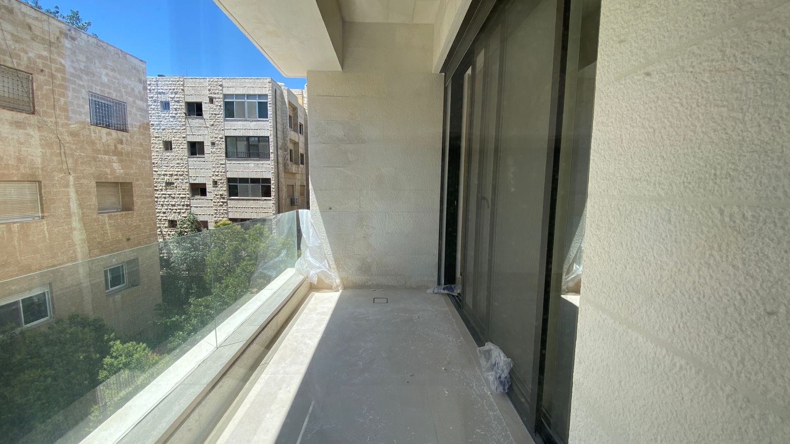 ba8fa870-28d0-48c4-aa1c-d25d6835a3b5 Balcony with glass railing overlooking neighboring beige stone buildings and a clear blue sky beyond.