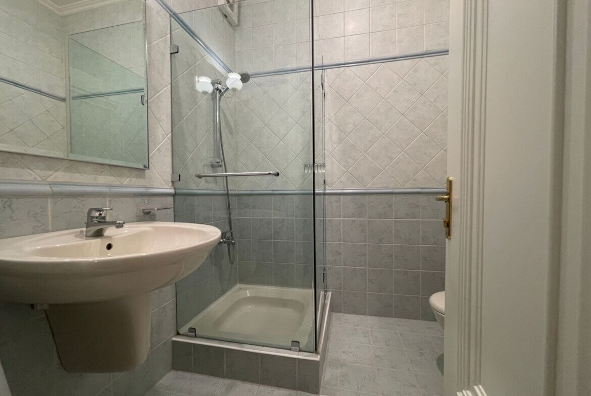 c3ef73e1-886d-4c4f-85a8-68bf77c7fe14 Small bathroom with a glass-enclosed shower, pedestal sink, and light-gray tiled walls.