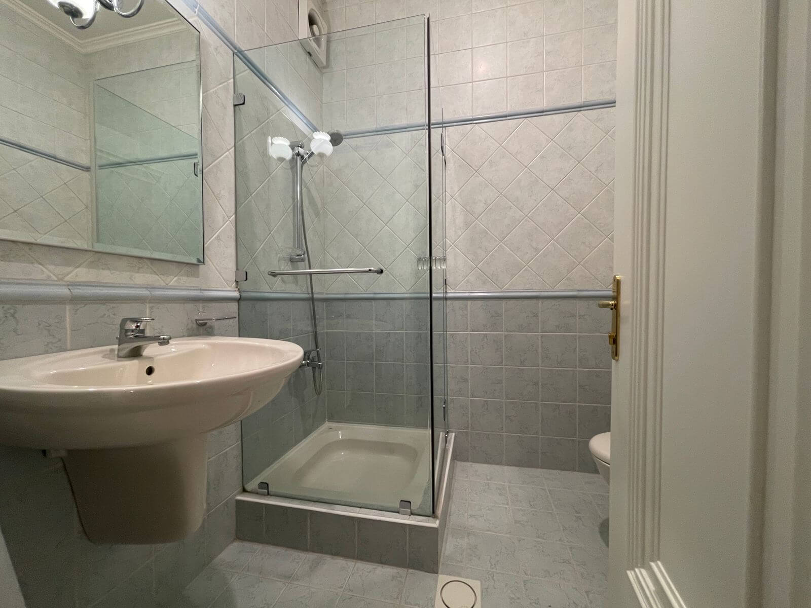 c3ef73e1-886d-4c4f-85a8-68bf77c7fe14 Small bathroom with a glass-enclosed shower, pedestal sink, and light-gray tiled walls.