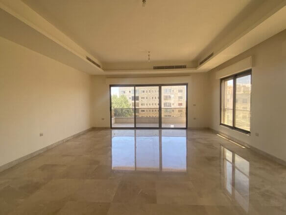 Bright empty living room with marble tile floor, neutral walls, and large sliding glass doors to a balcony showing nearby buildings.