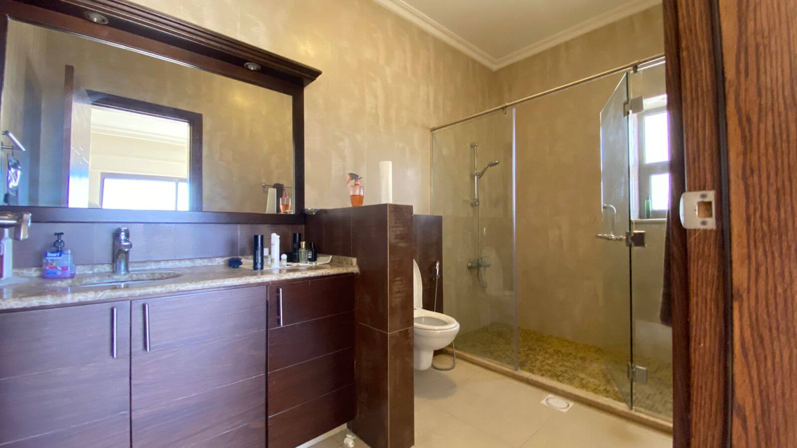 c8e5a28c-4fad-4e49-8cd1-e7c8a6060ca9 Modern bathroom with a dark wood vanity, marble countertop, large mirror, and a glass-enclosed shower.