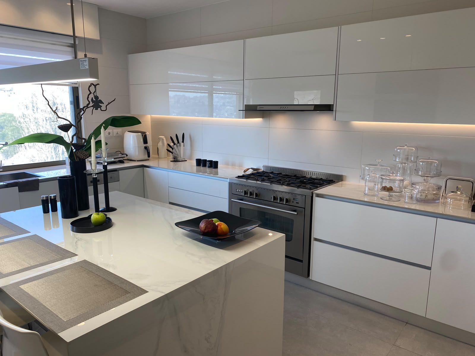 cd94f26e-4fb8-4049-a9ec-d724206736ae Modern white kitchen with marble island and stainless steel stove; bright under-cabinet lighting gives a clean, minimal look.