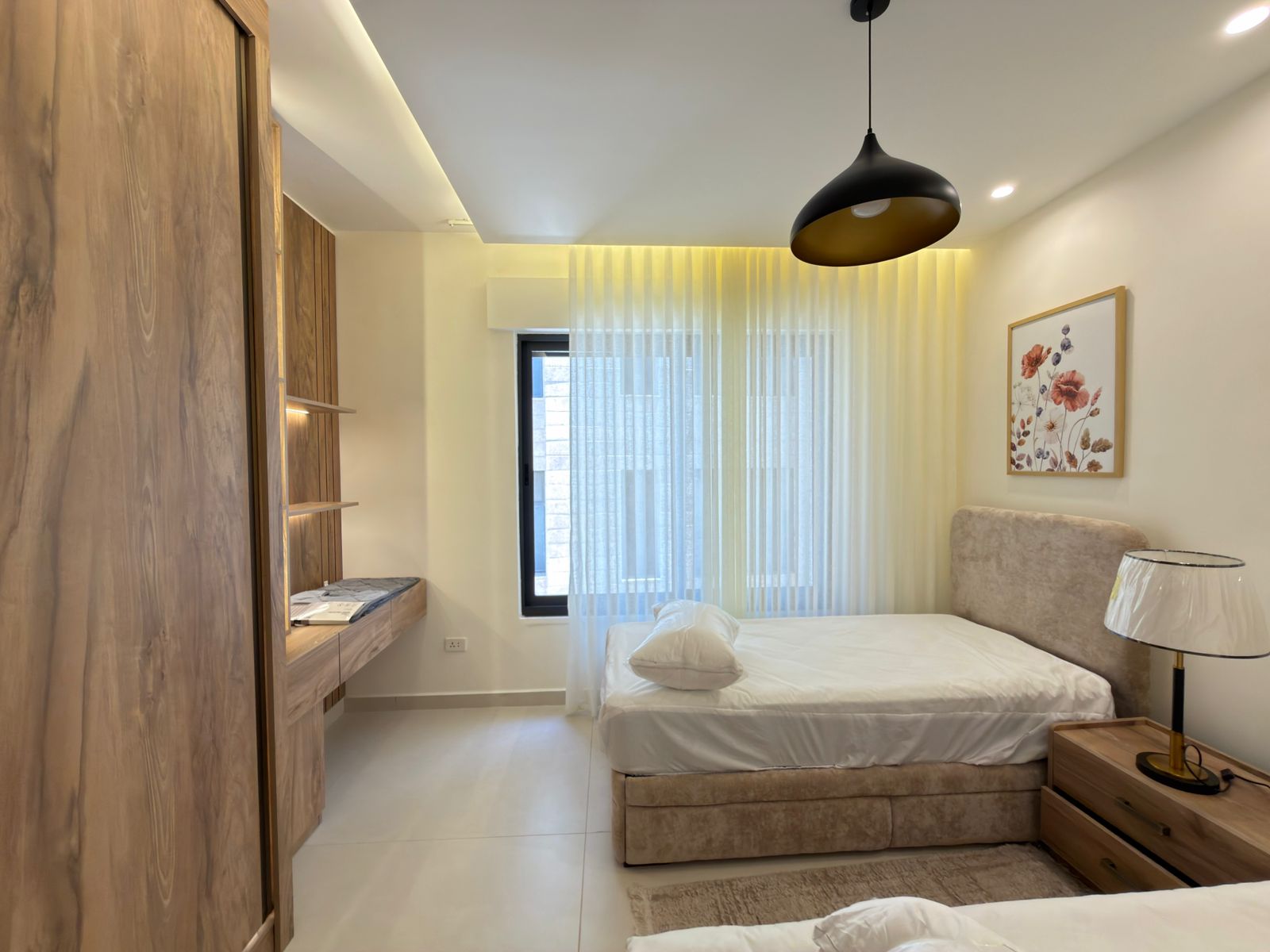 d1426dc9-aa3c-463e-a70a-de4147e606c5 Hotel bedroom with white bedding, beige upholstered headboard, wooden wardrobes, and a large window with sheer curtains.