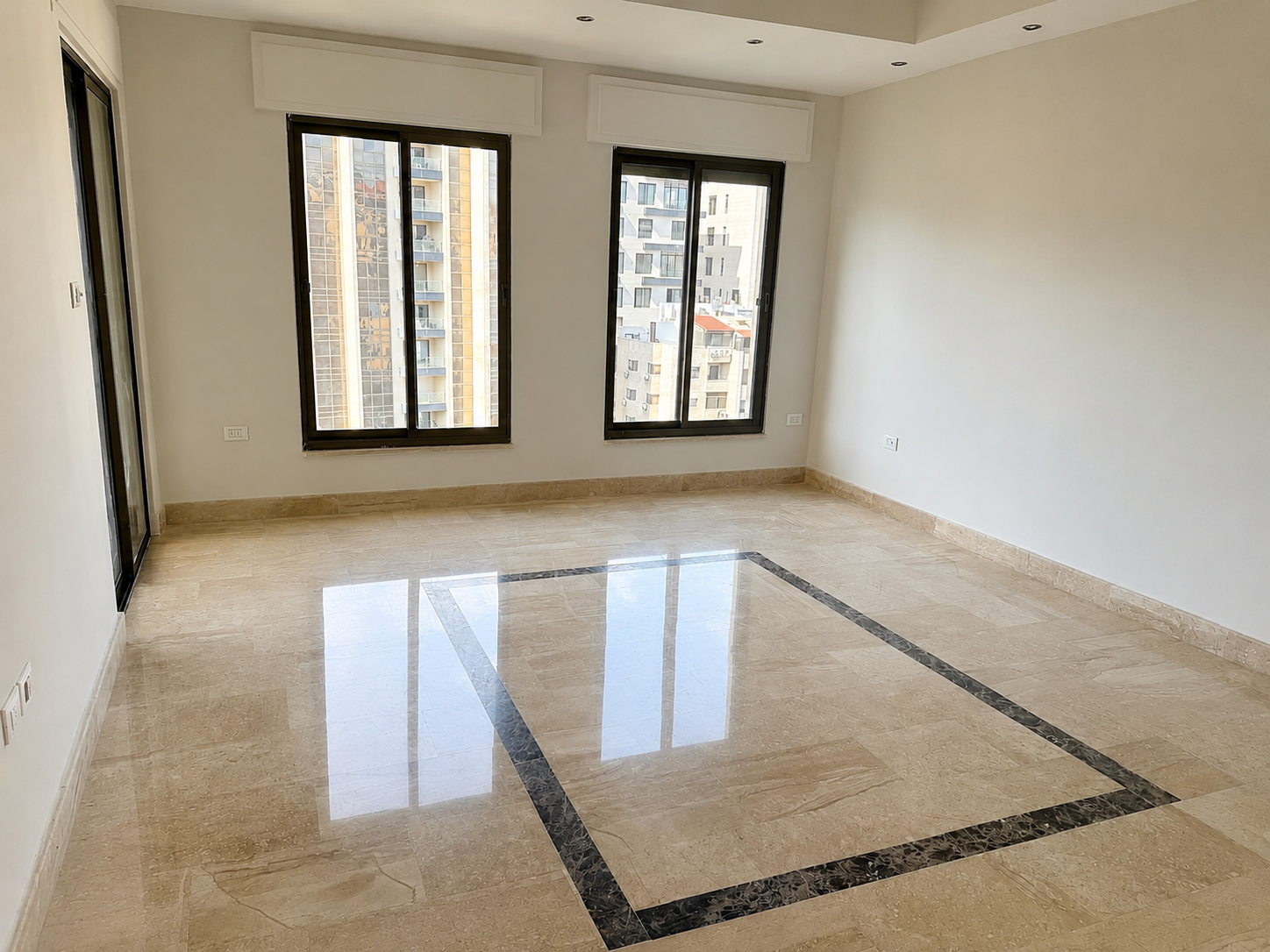 d5375eea-b9e2-4f41-aaa4-04010114e304 Empty living room with beige marble floor and a dark marble border, white walls, and large black-framed windows overlooking city buildings.