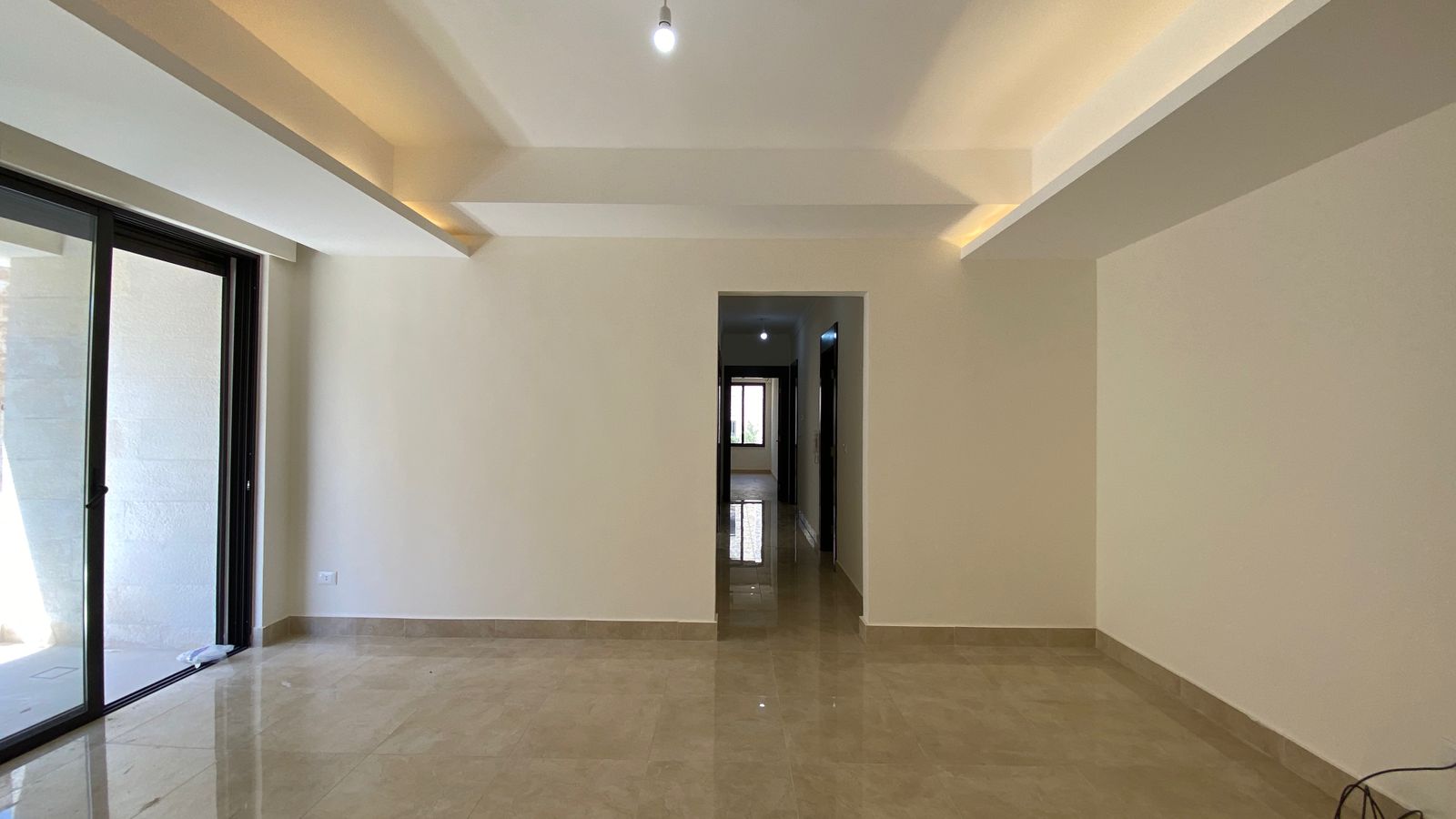 d6d16d07-40b3-4505-bcb3-405f42f55abb Empty modern living room with beige tiled floor and large sliding glass doors to the left; hallway straight ahead.