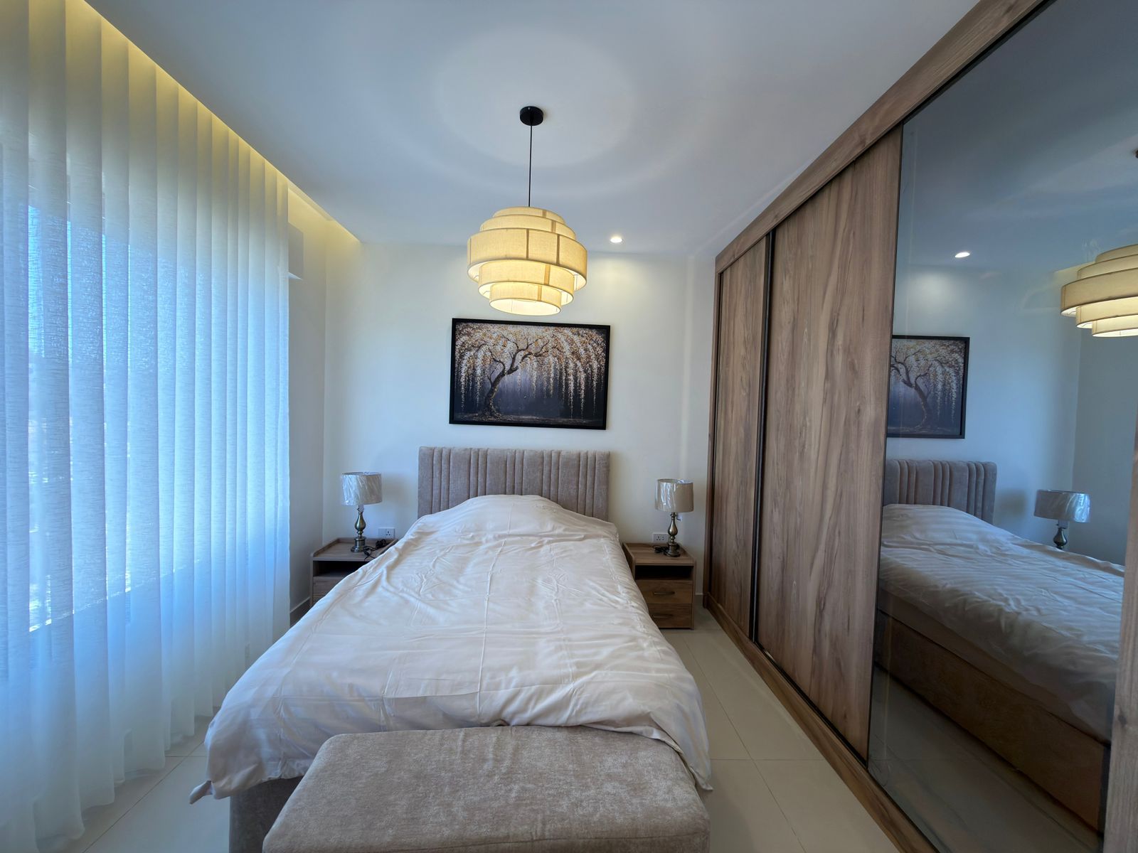 d870eb41-ee80-46c4-95cc-56fd1bc3cf10 Modern bedroom with white bedding, upholstered headboard, and a large wooden wardrobe with mirrored doors on the right.