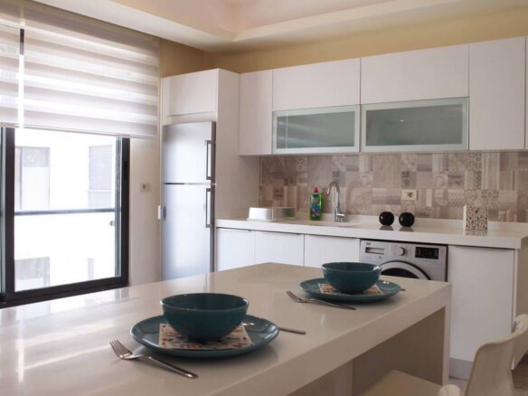 Bright modern kitchen with white cabinets, tiled backsplash, and a breakfast island set for two with teal bowls.