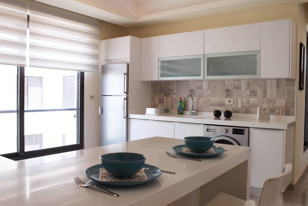 Bright modern kitchen with white cabinets, tiled backsplash, and a breakfast island set for two with teal bowls.