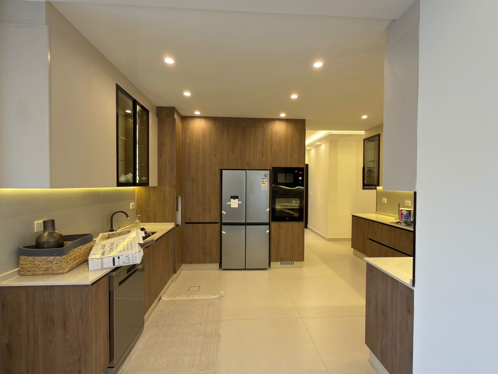 da7f4054-8a00-45ee-a7eb-3c823b6495b4 Modern kitchen with brown wood cabinets, stainless French-door fridge, built-in ovens, and under-cabinet lighting.