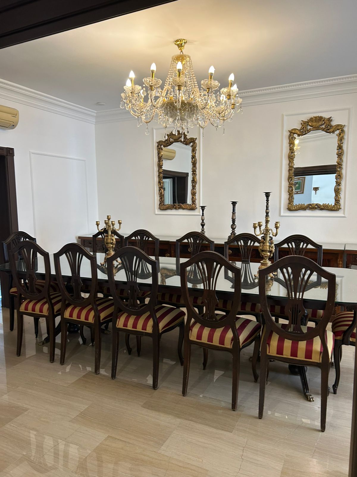 df7a9629-daaa-4018-84eb-813597bfd1de Elegant dining room with a glass-top table, dark wooden chairs, and a crystal chandelier overhead.