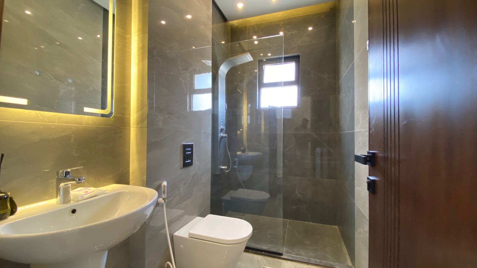 e0ded94b-2823-4779-8226-e75bdbc545d1 Modern bathroom with gray marble walls, a white pedestal sink, toilet, and a glass-enclosed shower.