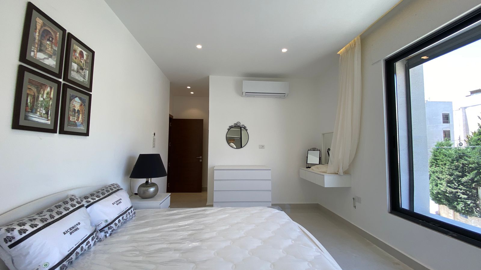 f3d3fbb0-fd57-462e-b5a2-e422ea5e17e7 Minimalist white bedroom with a large window, tufted bed, and black-lampside table beside the bed.