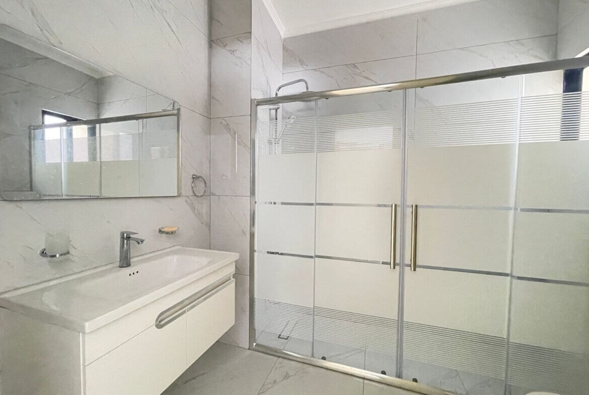 f5b69b38-3829-4166-b8e1-db2b256c78bd Bathroom with glass shower enclosure, chrome handles, and white vanity against marble-look walls and floor.