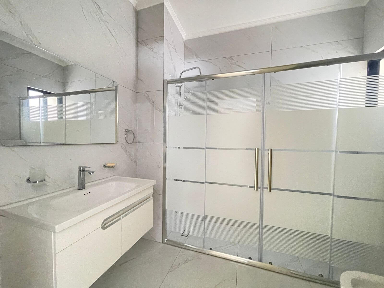 f5b69b38-3829-4166-b8e1-db2b256c78bd Bathroom with glass shower enclosure, chrome handles, and white vanity against marble-look walls and floor.