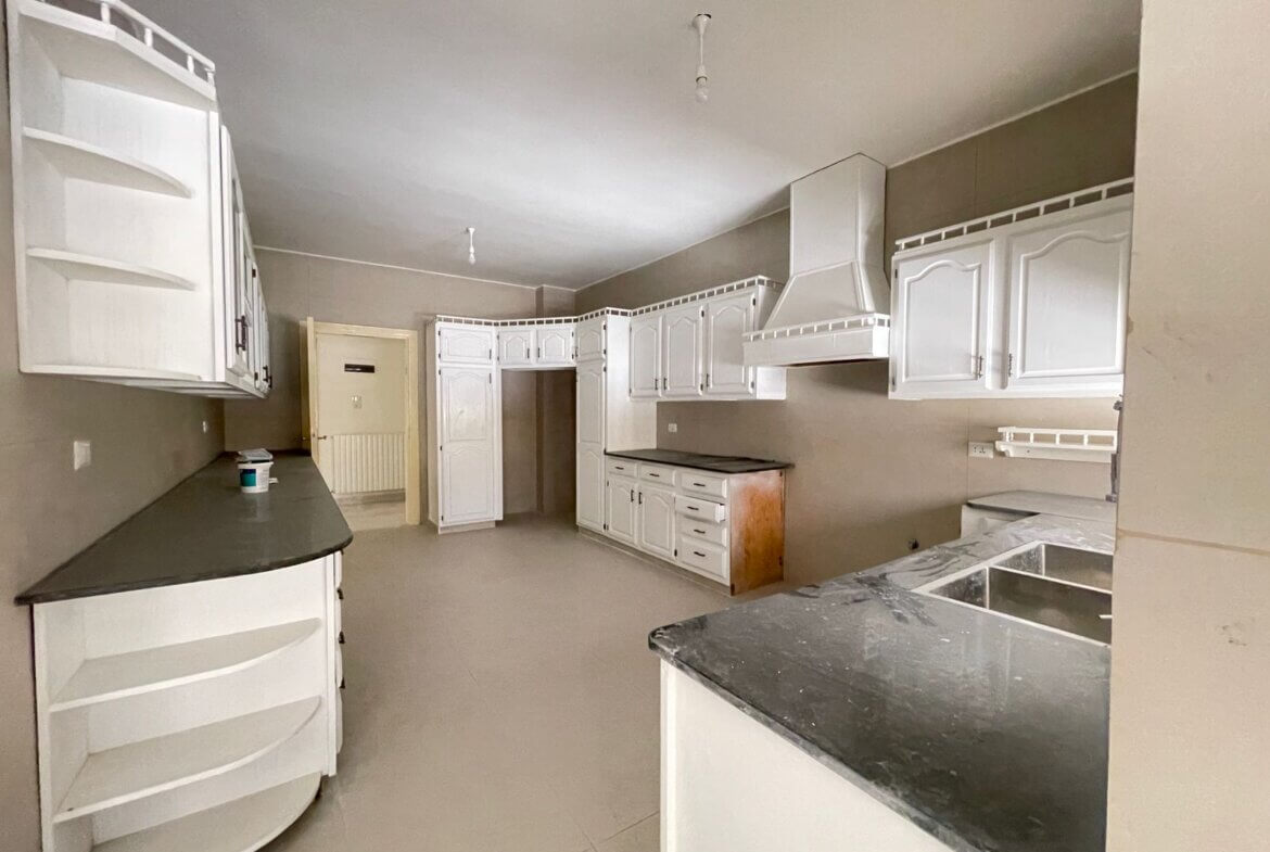 fa08b948-8d3a-4f3f-ba09-fb6a436c8c4a White L-shaped kitchen with tall white cabinets, dark countertops, and a large range hood along the back wall; empty and under-furnishing.