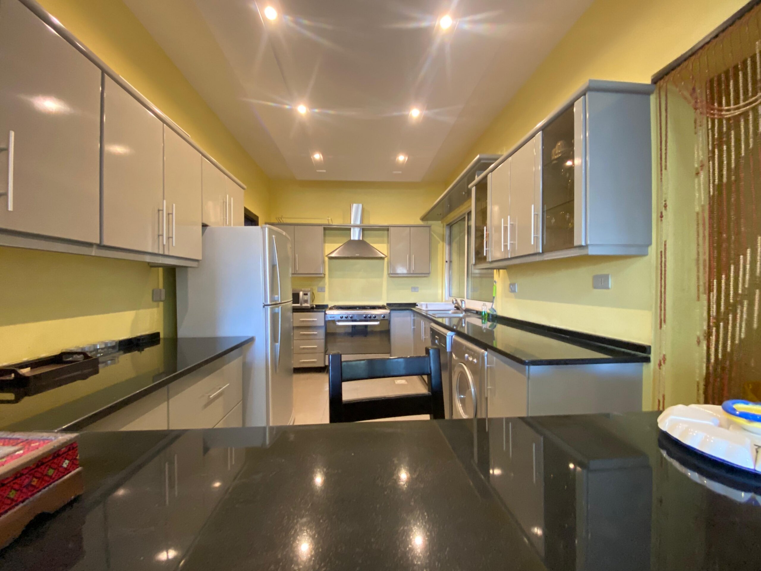 fcc36973-9322-4cfe-9603-95b65d2ed37c Modern kitchen with glossy grey cabinets, stainless steel fridge and stove, yellow walls, and black countertops.