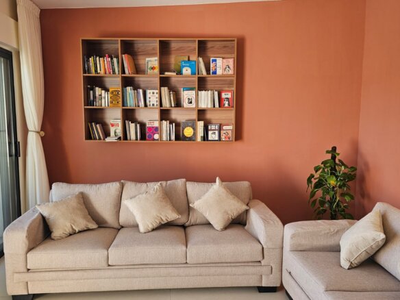 Living room with an orange accent wall, a wooden cubby bookshelf, and a beige sectional sofa with multiple cushions.