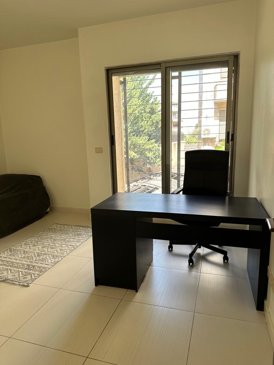 ff1a1de8-898d-43a9-a959-86a6f504f660 Home office with a dark wood desk and rolling chair by a sliding glass door to a balcony, tiled floor.